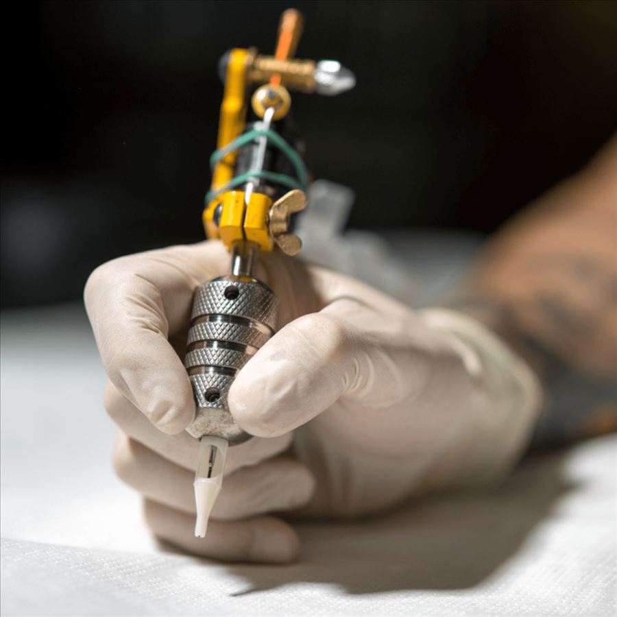 Gloved hand holding a tattoo machine
